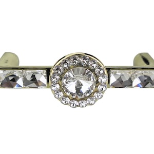 Könnte beinhalten: Goldfarbener Schrankknopf mit einem großen, klaren Kristall, der von kleineren Kristallen umgeben ist. Der Knopf hat eine rechteckige Basis mit klaren Kristallen.