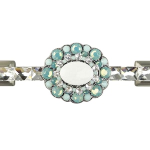 Può includere: Una maniglia per cassetto argentata con un centro ovale bianco circondato da un anello di strass blu chiaro e trasparenti.