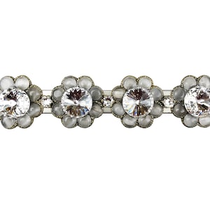 Könnte beinhalten: Eine silberne Haarklammer mit vier blütenförmigen Verzierungen. Jede Blüte hat eine klare Kristallmitte, die von kleineren, undurchsichtigen weißen Steinen umgeben ist.