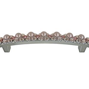 May include: A silver-toned cabinet pull with a curved shape and a decorative design of pink pearls and crystals.