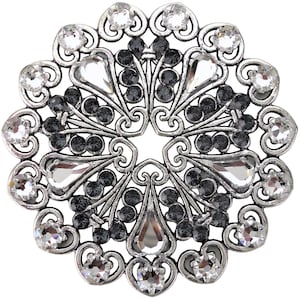 May include: A silver brooch with a circular design featuring black and clear rhinestones. The brooch has a delicate, intricate pattern with a floral motif.
