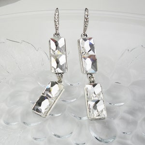 Puede incluir: Un par de pendientes de plata con piedras de cristal transparentes. Los pendientes tienen forma rectangular y están hechos de dos piedras apiladas.