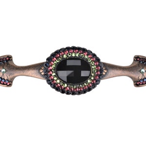 Op de afbeelding: Een decoratieve kastknop met een zwart kristallen middenstuk omgeven door een ring van gekleurde strass. De knop is gemaakt van metaal met een koperen afwerking en heeft aan beide uiteinden een puntig ontwerp.