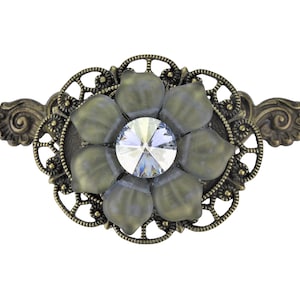 Könnte beinhalten: Eine Brosche im Vintage-Stil mit einem zarten Blumendesign und einem klaren Kristall in der Mitte. Die Brosche ist aus Metall mit einer antiken Messing-Oberfläche und hat ein detailliertes Filigran-Design.