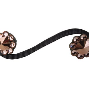 Puede incluir: Una liga para el pelo de cuero negro con dos adornos de cristal. Cada adorno es un círculo de pequeños cristales transparentes que rodean un cristal más grande de color rosa dorado.