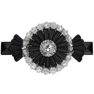 Könnte beinhalten: Schwarzer Haarklammer mit einem großen, runden, mit Kristallen besetzten Blumendesign. Die Blume hat einen großen, klaren Kristall in der Mitte, umgeben von kleineren, schwarzen, fächerförmigen Teilen.