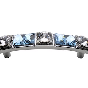 Puede incluir: Un tirador de armario plateado con un diseño curvo y cuatro acentos de cristal. Dos de los cristales son transparentes y dos son azul claro.