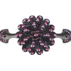 May include: A dark gray metal drawer pull with a decorative flower design. The flower is made of small, dark red crystals.