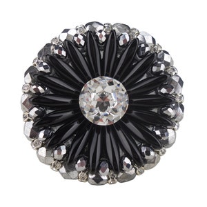 Op de afbeelding: Een zwarte en zilveren broche met een groot kristal in het midden en een bloemmotief.