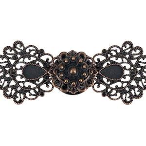 Może przedstawiać: Antyczne zapięcie w odcieniu brązu z misternymi detalami filigranowymi. Zapięcie posiada centralny owalny wzór z motywem kwiatowym, otoczony dwoma ozdobnymi, ażurowymi panelami. Całkowity projekt jest symetryczny i dekoracyjny.