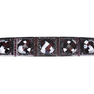 Puede incluir: Una pulsera negra con cinco piedras preciosas grandes, facetadas, de color rojo oscuro engastadas en un marco de metal plateado.