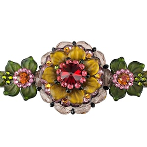 Könnte beinhalten: Eine Blumen-Haarklammer mit einer großen gelben Blume in der Mitte, umgeben von kleineren rosa und grünen Blumen. Die Blumen sind aus Glas und haben einen glitzernden Überzug.