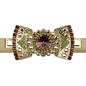 Könnte beinhalten: Eine goldene Haarklammer mit einem großen, mehrfarbigen, braunen Kristall in der Mitte. Die Klammer ist mit kleineren Kristallen in Grün-, Braun- und Rosatönen verziert, die in einem geometrischen Muster angeordnet sind.