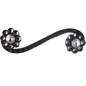 Puede incluir: Una pinza para el pelo negra con dos adornos decorativos en forma de flor. Cada flor tiene un centro de cristal de roca transparente rodeado de cristales de roca negros.