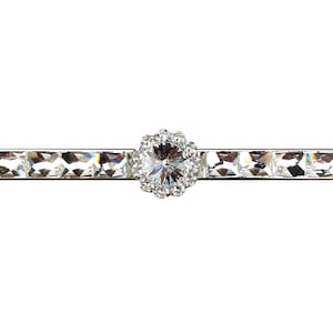 Może przedstawiać: Srebrna listwa z dużym, przezroczystym kryształem w środku, otoczonym mniejszymi, przezroczystymi kryształami. Listwa jest ozdobiona mniejszymi, przezroczystymi kryształami.