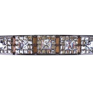 Può includere: Un fermaglio per capelli argentato con una fila di cristalli quadrati trasparenti e cristalli più piccoli in un motivo geometrico.