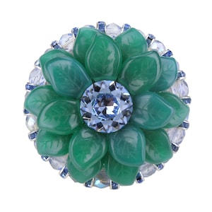 May include: A green flower brooch with a blue crystal centre surrounded by clear and blue rhinestones.
