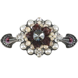 Può includere: Un fermaglio d'argento con un grande motivo floreale marrone scuro. Il fiore ha un cristallo grigio scuro al centro ed è circondato da perle bianche e strass trasparenti. Il fermaglio ha due anelli d'argento su entrambi i lati.