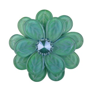 Peut inclure: Une broche en forme de fleur verte avec un grand cristal transparent au centre. La fleur est composée de plusieurs couches de pétales, chacune d'une nuance de vert légèrement différente.