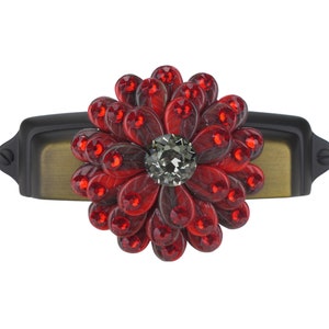Op de afbeelding: Een rode en zwarte, met juwelen bezette, bloemvormige kastknop met een zwarte en gouden basis.