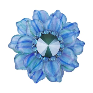 Peut inclure: Une broche en forme de fleur en verre bleu avec un grand cristal vert foncé facetté au centre. La fleur a un motif rayé et est entourée de petits cristaux bleus.