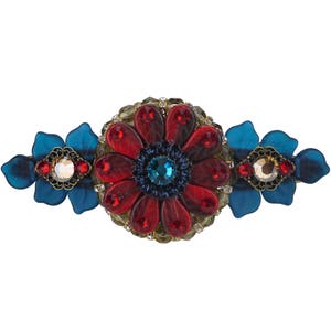 Op de afbeelding: Een rode en blauwe broche met juwelen in de vorm van een bloem, met een grote rode bloem in het midden en twee kleinere blauwe bloemen aan weerszijden.