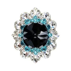 May include: A large black crystal surrounded by smaller clear and turquoise crystals, set in a silver tone metal base. The crystals are arranged in a flower shape.