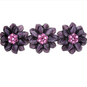 Puede incluir: Tres pinzas para el pelo de color morado con forma de flor y detalles de pedrería rosa.