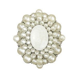 May include: A white oval-shaped stone surrounded by a cluster of white pearl-like beads, forming a decorative brooch.