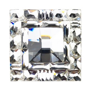 Könnte beinhalten: Ein quadratischer Kristallknauf mit facettiertem Design. Der Knauf hat einen klaren Kristallrahmen mit einem kleineren, dunkleren Kristallquadrat in der Mitte.