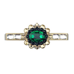 May include: A gold-toned barrette featuring an oval, emerald-green gemstone surrounded by a floral design of black, gold, and clear crystals. The barrette has clear rectangular crystals on each end.