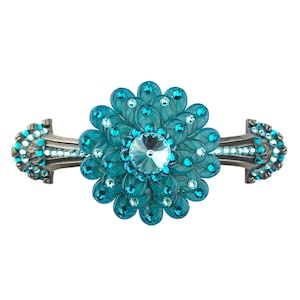 Può includere: Una maniglia decorativa per armadi con un design floreale. Il centro del fiore è un grande cristallo blu chiaro rotondo. I petali sono di colore turchese traslucido e l'hardware è di colore argento scuro. Piccoli cristalli trasparenti sono incastonati attorno al fiore.