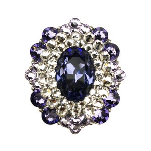 以下が含まれることがあります： 周囲をより小さな透明と紫のラインストーンで囲まれた、大きな楕円形の濃い青色のラインストーン