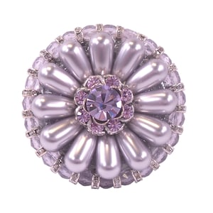 Puede incluir: Un broche de flor plateado y morado con un gran cristal central rodeado de cristales más pequeños. La flor está hecha de perlas falsas.