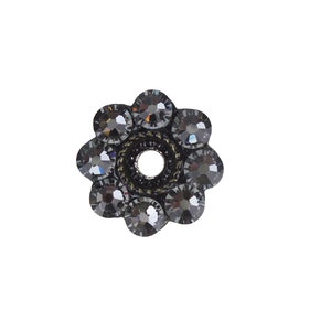 May include: A black flower-shaped bead with a hole in the center. The bead is made of metal and has a shiny finish. It is decorated with small, black rhinestones.
