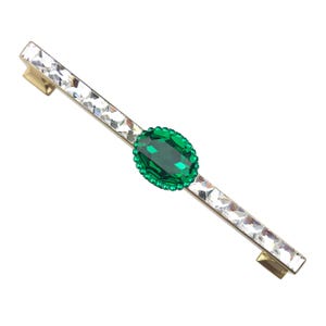 Op de afbeelding: Een goudkleurige kastgreep met een centraal ovaalvormig smaragdgroen juweel, omringd door kleinere groene stenen. De greep is versierd met heldere, rechthoekige kristallen.