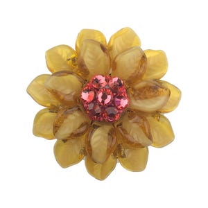 May include: A floral brooch featuring multiple amber-colored, leaf-shaped glass petals arranged in layers. The center of the flower is composed of a cluster of small, round, bright pink faceted crystals that catch the light.