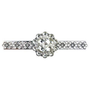 Puede incluir: Horquilla plateada con un gran centro de pedrería transparente y redondo, rodeado de pedrería más pequeña. Los lados de la horquilla están adornados con grupos de pedrería transparente, creando un accesorio brillante y elegante.