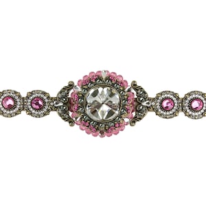 Może przedstawiać: Dekoracyjna spinka do włosów z dużym, przezroczystym kryształem otoczonym różowymi i srebrnymi koralikami. Spinka ma złote wykończenie i jest ozdobiona misternymi detalami.