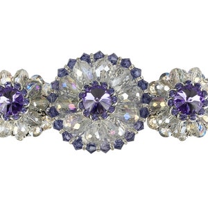 Puede incluir: Una pinza para el pelo de plata con tres racimos de flores de cristales transparentes y morados.