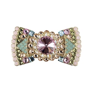May include: A rectangular brooch featuring a large central pink faceted crystal surrounded by smaller clear, pink, and olive green crystals. The gold-tone metal frame is accented with light blue square stones and pale pink round cabochons.