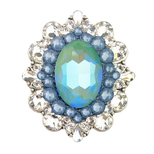 Peut inclure: Broche ornée d'une pierre ovale bleu-vert irisée, entourée de petites pierres bleues et de cristaux transparents. Le sertissage est de couleur argentée. Le design est orné et accrocheur, adapté aux tenues de soirée ou pour ajouter de l'éclat.