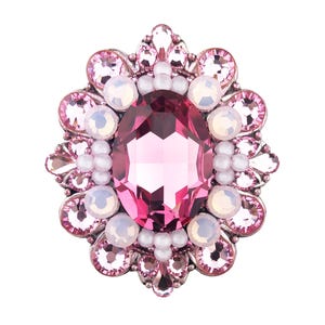 May include: A pink and silver brooch featuring an oval, faceted pink central stone. The brooch is encircled by smaller pink and white stones, and white pearl-like beads. The setting is silver-coloured metal.