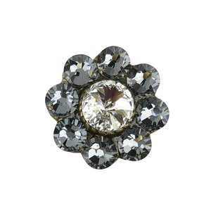 Puede incluir: Una decoración en forma de flor plateada con un centro de cristal transparente y ocho cristales gris oscuro que la rodean.