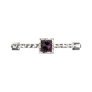 May include: A horizontal bar brooch featuring a central square setting with a deep purple faceted stone surrounded by small purple crystals. The elongated arms are lined with clear, rectangular faceted crystals set in a polished silver-tone metal.