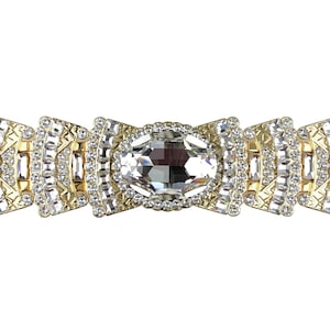 May include: A gold-toned bracelet with a large, clear crystal centerpiece surrounded by smaller crystals. The bracelet is made of metal and has a geometric design.