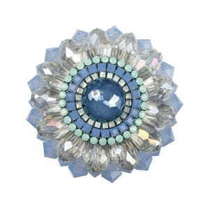 May include: A circular brooch featuring a large, smooth, dark blue central cabochon surrounded by concentric rings of light blue square crystals, mint green round beads, and an outer layer of faceted, clear, and pale blue crystal petals.