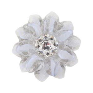 Pode incluir: Um broche em forma de flor com pétalas de vidro transparente e branco translúcido dispostas em várias camadas. No centro do design floral, encontra-se um cristal único, redondo e facetado, que reflete a luz com uma superfície brilhante.