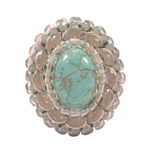 以下が含まれることがあります： 銀色の枠にターコイズの宝石がセットされたリング。リングは虹色の白と薄い青のビーズの輪で囲まれています。