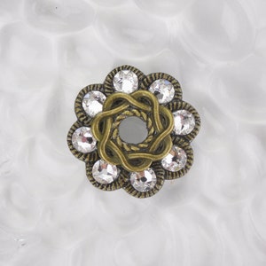 以下が含まれることがあります： クリアなラインストーンが付いた、ゴールドトーンの金属製のフラワーシェイプの装飾。花の真ん中には円形の開口部があります。